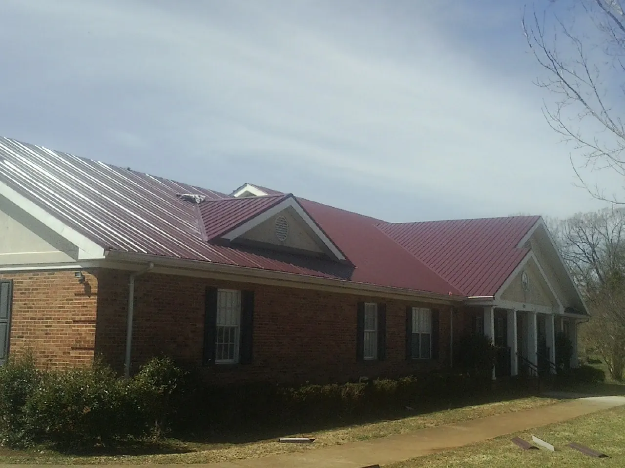 Red metal roof with gabled entries on a long brick building, from a Hail Damage Roof Repair job in Essex Junction