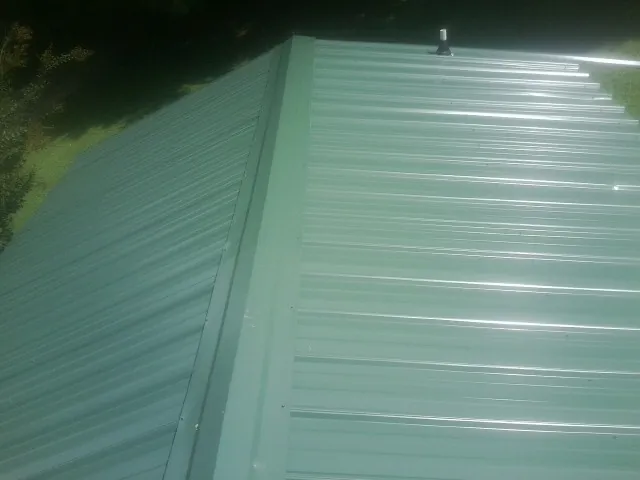 New green metal panels meeting at the ridge of a roof — Flat Roof Repair work by our crew in Essex Junction