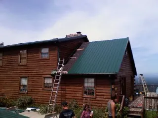 Green metal roof going on a two story log home with ladders set in Essex Junction