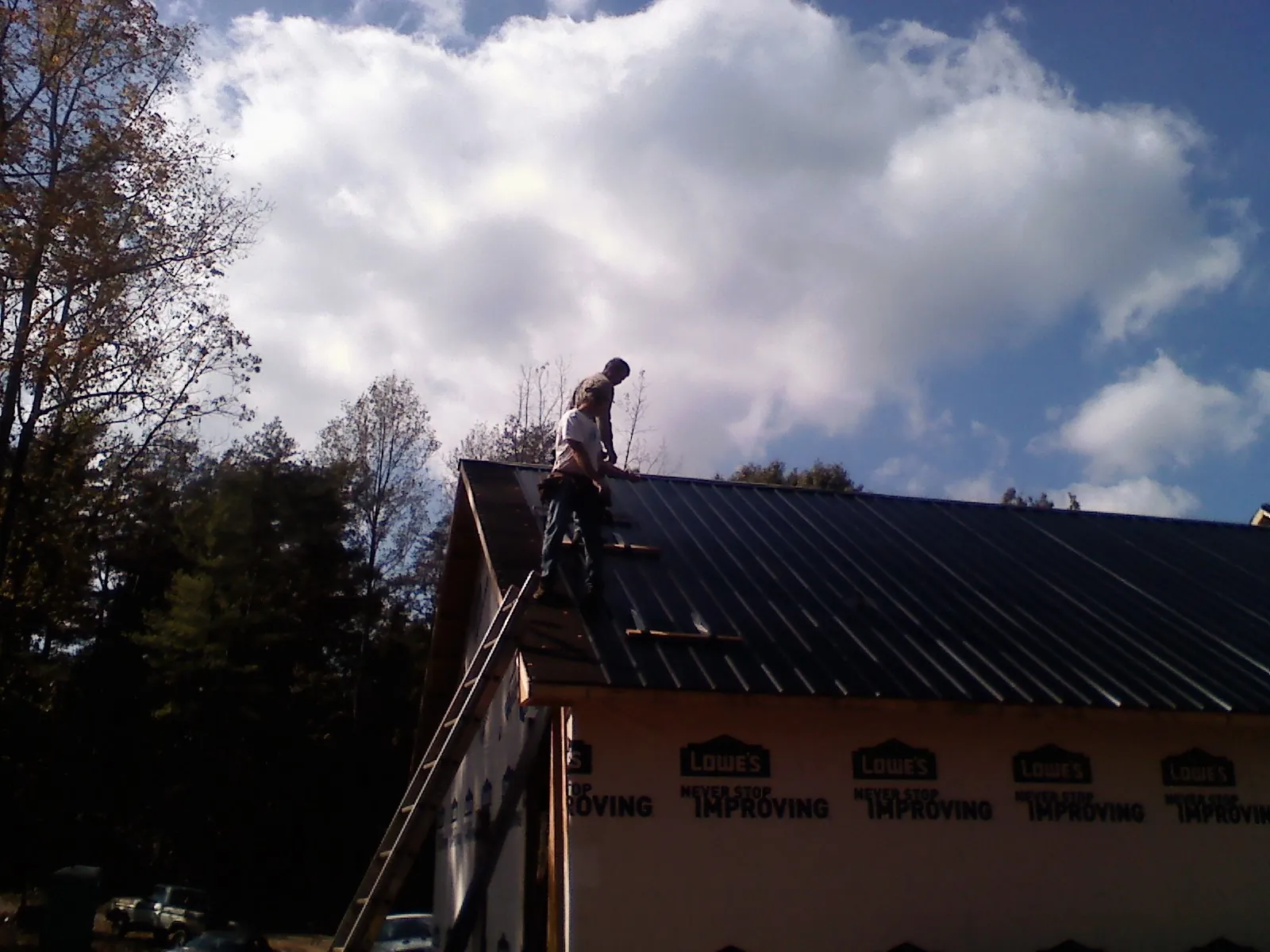 Roofer fastening dark metal panels high against a cloudy sky, from a Roof Inspection job in Essex Junction