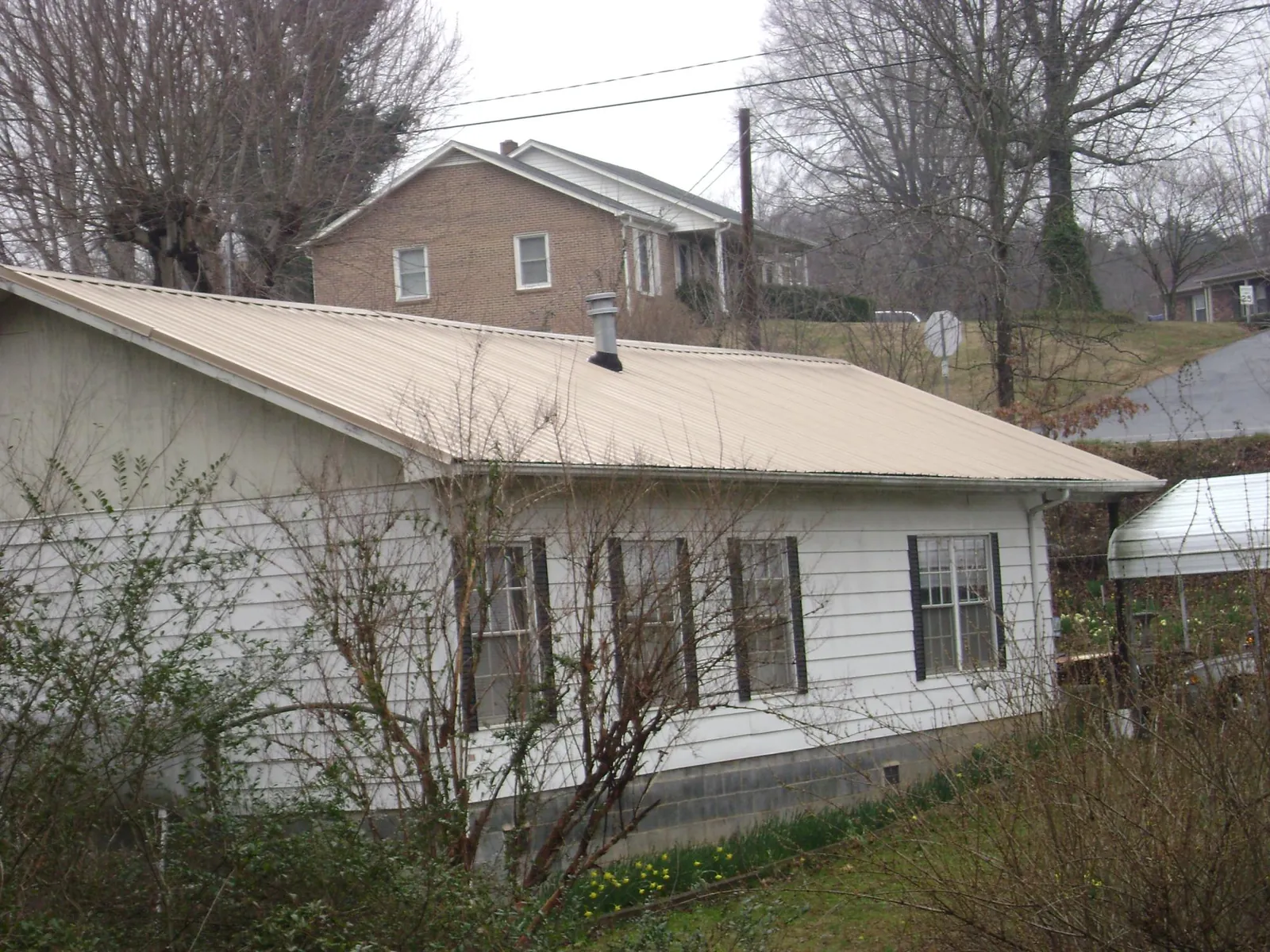 Tan metal roof on a white sided house set into a hillside — Commercial Roofing by Roofing Brothers in Essex Junction