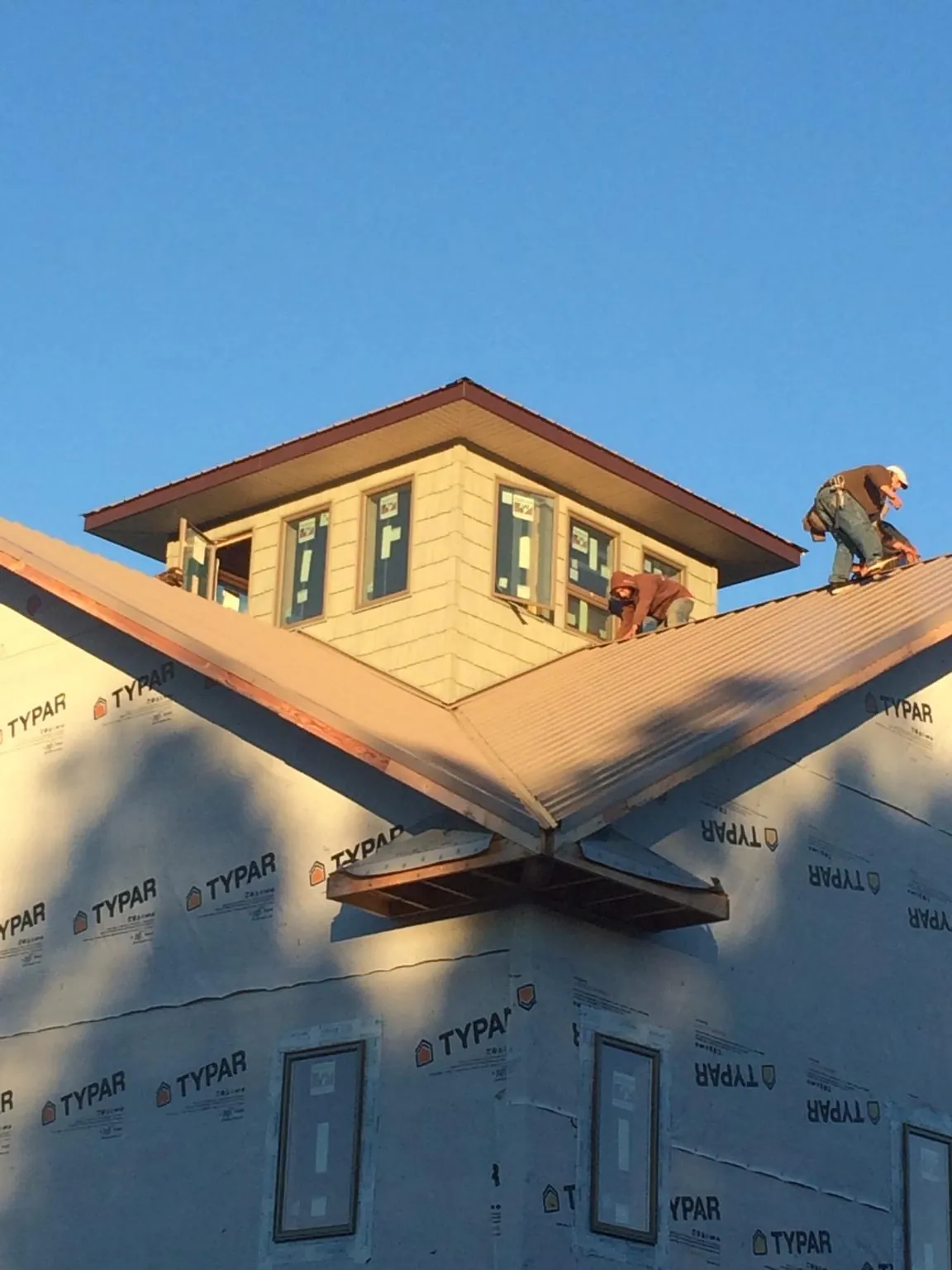 Roofers working around a rooftop cupola on a new metal roof at sunset — Roof Waterproofing in Essex Junction by Roofing Brothers